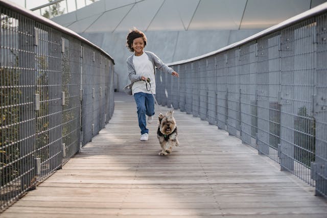 Happy ethnic boy running on bridge with cute dog